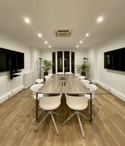 Salle de réunion moderne équipée d'un système de visioconférence avec table centrale et chaises blanches