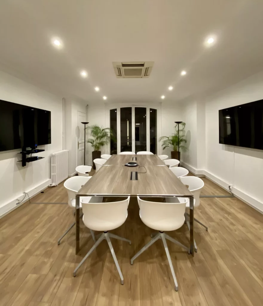 Salle de réunion moderne équipée d'un système de visioconférence avec table centrale et chaises blanches