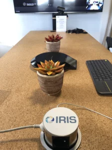 Salle de réunion équipée d'un système de conférence audio IRIS avec table de bois, plantes décoratives et écran de présentation pour visioconférences professionnelles