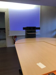 Salle de conférence moderne équipée pour visioconférences avec système Neat compatible Google Meet, grand écran et table de réunion épurée