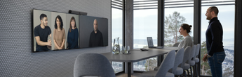 Réunion professionnelle dans un espace de travail moderne avec participants en présentiel et visioconférence sur écran mural, conformément aux dispositions relatives aux assemblées délibérantes.