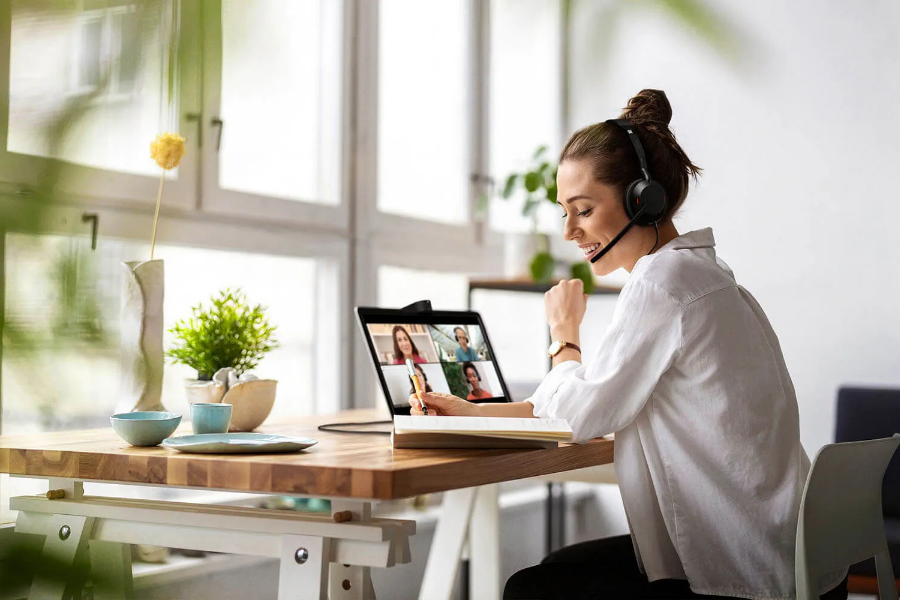 Jeune femme souriante avec un casque audio en train de faire une visioconférence sur son ordinateur portable dans un bureau moderne.