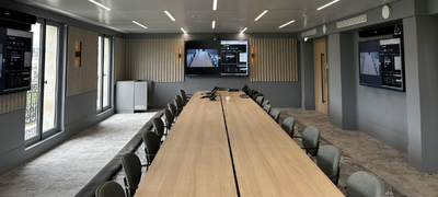 Grande salle de conférence équipée de multiples écrans et d'un système de visioconférence IRIS Connect pour des présentations et réunions d'envergure.